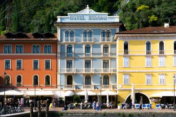A row of colorful multi-story buildings along a waterfront promenade, with the central white building displaying "HOTEL EUROPA" signage, outdoor café seating, and bicycles parked in front.