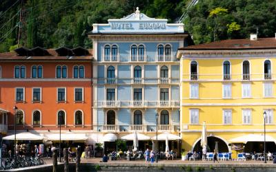 A row of colorful multi-story buildings along a waterfront promenade, with the central white building displaying "HOTEL EUROPA" signage, outdoor café seating, and bicycles parked in front.