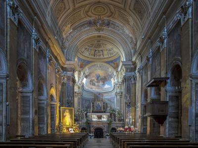 The interior of a grand Baroque-style church featuring marble columns, an ornate vaulted ceiling, a large apse painting, and a prominent golden statue of the Virgin Mary on the left side.