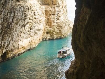 A view from inside a sea cave looking out at a white tour boat navigating turquoise water between towering, light-colored limestone cliffs.