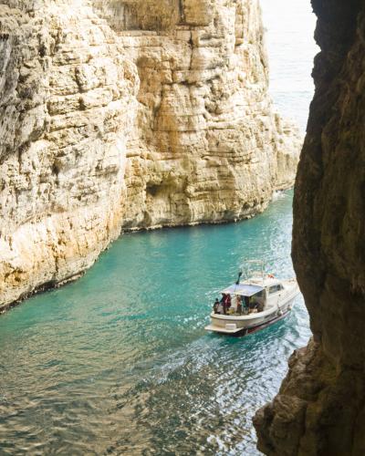 A view from inside a sea cave looking out at a white tour boat navigating turquoise water between towering, light-colored limestone cliffs.