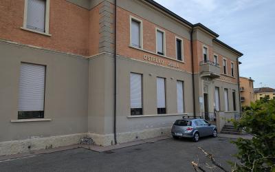 The image shows the exterior of a two-story building with brick and stucco facade, featuring signage that reads "OSTELLO DELLA GIOVENTU" above the entrance, with a silver car parked in front and greenery to the right.