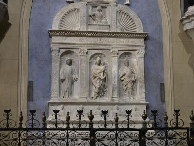 A detailed white marble funerary monument or tomb effigy set within a blue-painted arched niche, featuring multiple sculpted figures and enclosed by a black wrought-iron fence.