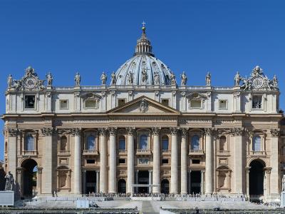 A frontal view of St. Peter's Basilica in Vatican City, showing its grand Baroque facade with Corinthian columns, statues along the roofline, the central dome by Michelangelo, and the Latin inscription "IN HONOREM PRINC APOST PAVLVS V BORGHESIVS R