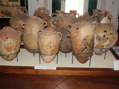 A display of large, ancient, repaired ceramic amphorae and jars on metal stands within a museum setting, with informational placards visible.