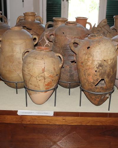 A display of large, ancient, repaired ceramic amphorae and jars on metal stands within a museum setting, with informational placards visible.