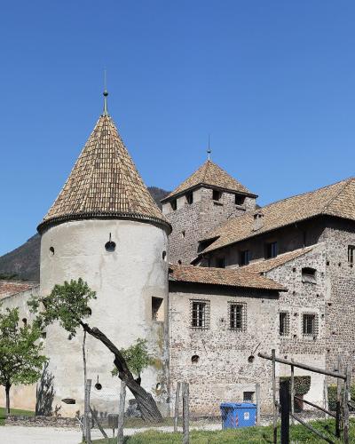 A stone castle with multiple conical-roofed towers and a central building, set against a clear blue sky with hills in the background; no visible signage or text.
