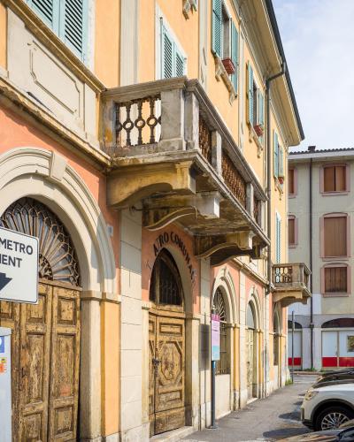 The image shows the exterior of a building with arched wooden doors and a balcony, featuring signage that reads "TEATRO COMUNALE" above an entrance, located on a street with parked cars and a directional sign for "METRO" (likely indicating a metro