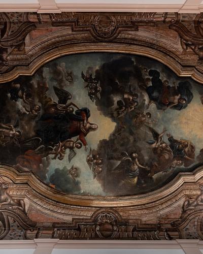 An interior ceiling fresco featuring a central oval painting of religious figures amidst clouds, surrounded by ornate trompe-l'œil architectural stucco work and two circular medallions containing black birds.