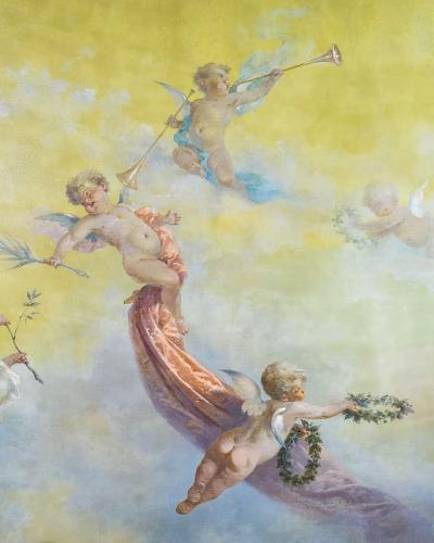 The image shows a classical-style fresco painting featuring several cherubs (putti) in flight against a soft yellow and blue sky, holding musical instruments, laurel wreaths, and ribbons.