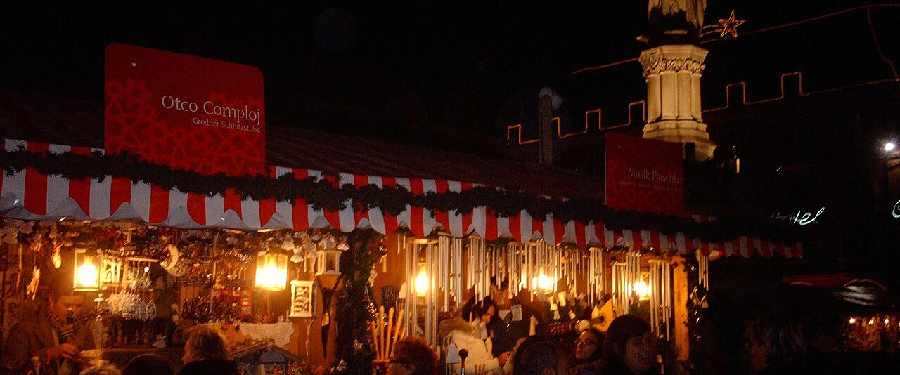 Christmas market stalls lit up at night in Piazza Walther, Bolzano, below the statue of Walther von der Vogelweide