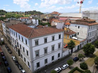 An elevated view of a large, white, multi-story building with a terracotta-tiled roof situated at a street corner, with a construction crane and scaffolding visible on an adjacent structure to the right.