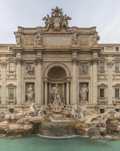 The image shows the Trevi Fountain in Rome, Italy, featuring its grand Baroque architecture with statues of Oceanus, allegorical figures, and cascading water into a large basin, surrounded by tourists and adjacent buildings.
