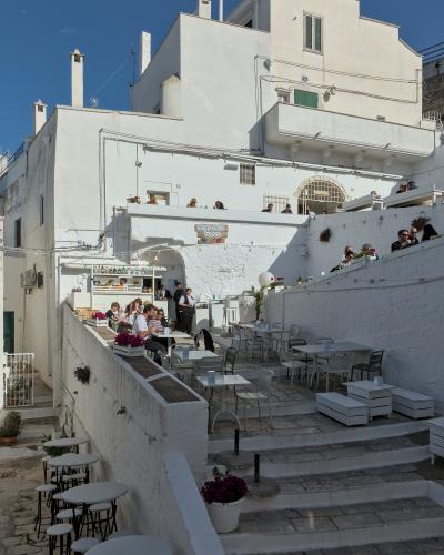 The image shows an outdoor terrace of a restaurant or bistro named "Borgo Antico Bistrot," featuring white-washed buildings, stone steps, and patrons dining under a clear blue sky.