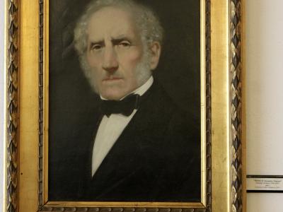 A framed oil portrait of an elderly man with white hair and sideburns, wearing a black suit and bow tie, hanging on a white wall; a small museum label to the right reads “Ritratto di Alessandro Manzoni” by Giuseppe Molteni (1805–1867), dated 1867,