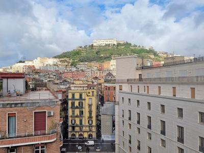 A view of the Naples cityscape looking up toward the Vomero hill, where the large white building complex of the Certosa di San Martino is visible at the summit.