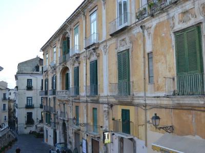 A weathered, multi-story yellow building with green shutters and balconies on a sloping street in an Italian town, with a sign for "Cafeteria" visible at the bottom right.