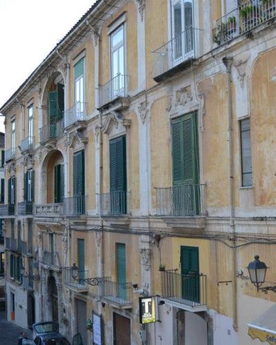 A weathered, multi-story yellow building with green shutters and balconies on a sloping street in an Italian town, with a sign for "Cafeteria" visible at the bottom right.