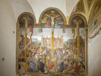 A large, damaged fresco depicting the Crucifixion of Christ flanked by two other crucified figures, with crowds and architectural elements in the background, painted on an interior wall within an arched alcove.