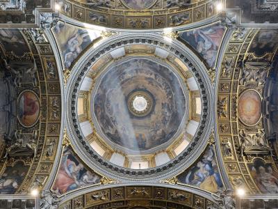The image shows the ornate, frescoed dome interior of a grand church, featuring a central oculus, gilded architectural details, and Baroque-style paintings of figures in the sky.