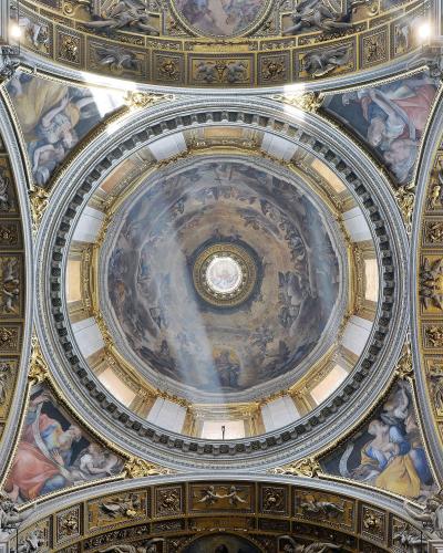 The image shows the ornate, frescoed dome interior of a grand church, featuring a central oculus, gilded architectural details, and Baroque-style paintings of figures in the sky.