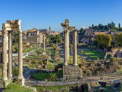 A panoramic view of the Roman Forum archaeological site in Rome, featuring prominent ancient ruins like the Temple of Saturn columns and the Arch of Septimius Severus, with the Church of Santi Luca e Martina visible on the left and the Capitoline