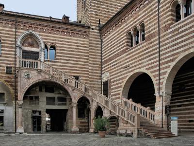 The image shows the Scala della Ragione (Reason's Staircase) and the Palazzo della Ragione in Verona, Italy, characterized by its distinctive red-and-white striped brickwork and a grand external stone staircase.