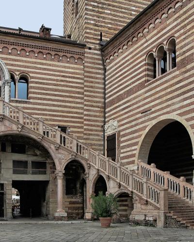 The image shows the Scala della Ragione (Reason's Staircase) and the Palazzo della Ragione in Verona, Italy, characterized by its distinctive red-and-white striped brickwork and a grand external stone staircase.