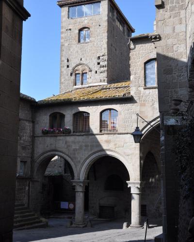 A stone courtyard with arched colonnades, a tall medieval tower with arched windows, and historic buildings under a clear blue sky; no visible signage or text identifying the location.