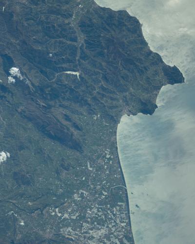 A high-altitude satellite or orbital photograph showing a rugged, mountainous coastline with a prominent peninsula jutting into the sea, a large inland lake (Lago Alento), and a flat coastal plain with agricultural fields and urban development nea