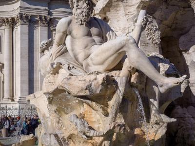 A close-up view of the Fontana dei Fiumi (Fountain of the Rivers) in Piazza Navona, Rome, featuring Gian Lorenzo Bernini's statue of the Nile river god with a rocky base and water flowing into the basin, with the facade of the Church of Sant'Agnes