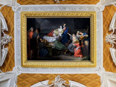 A view of an ornate interior ceiling and upper wall featuring three large, gilded-framed paintings set against a gold-leaf coffered ceiling with white stucco architectural details.