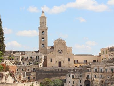 A wide-angle photograph of a large stone cathedral with a tall, square bell tower and a rose window, situated on a hilltop amidst other historic buildings under a blue sky.