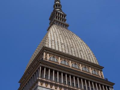 A low-angle photograph of a large, ornate building with a distinctive copper-clad dome and a tall, slender spire topped with a star, set against a clear blue sky.