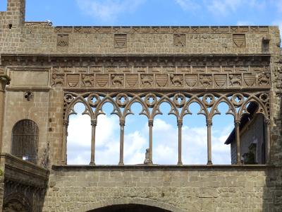 The image shows the upper loggia and facade of the Palazzo dei Papi in Viterbo, featuring a distinctive Gothic-style open gallery with pointed arches and a frieze of carved shields and lions.