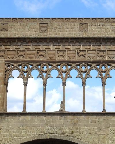 The image shows the upper loggia and facade of the Palazzo dei Papi in Viterbo, featuring a distinctive Gothic-style open gallery with pointed arches and a frieze of carved shields and lions.
