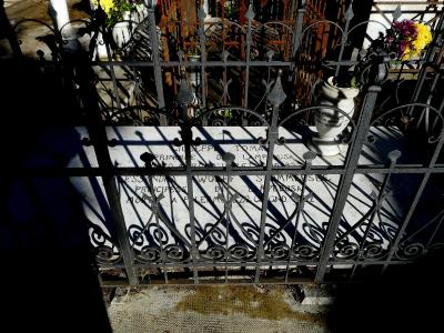 A close-up view of a white marble tombstone behind a black wrought-iron fence, with inscriptions for "GIUSEPPE TOMASI PRINCE DI LAMPEDUSA" and "ALESSANDRA WOLFF STEMMER PRINCESSA DI LAMPEDUSA".