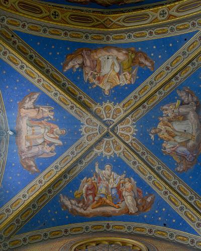 The image shows an ornate, vaulted ceiling with blue starry frescoes, painted figures on clouds, gilded architectural ribs, a rose window, and part of a pipe organ.