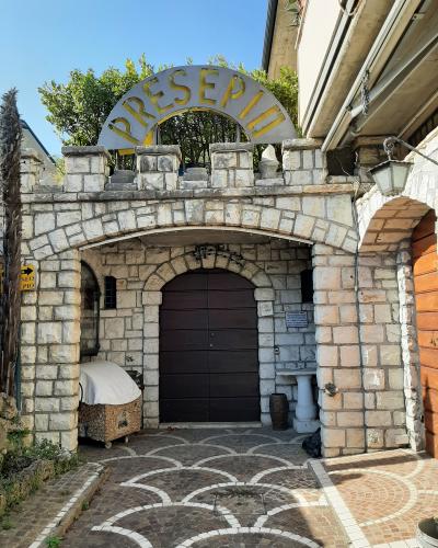 The image shows the stone entrance archway of a building with a large arched sign reading "PRESEPIO" in gold letters, a dark wooden gate, and a paved courtyard with a scalloped tile pattern.