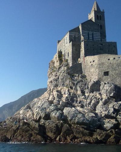 The image shows the Church of San Pietro perched on a rocky promontory overlooking the sea, with a distinctive striped facade and bell tower, located in Portovenere, Italy.