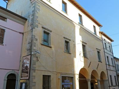 A yellow multi-story building with a corner rusticated stone detail, arched loggia on the ground floor, and a sign reading "UFFICIO INFORMAZIONE TURISTICA" (Tourist Information Office) on the glass door.