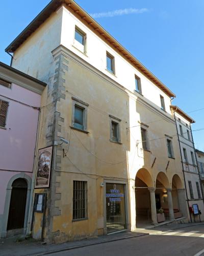 A yellow multi-story building with a corner rusticated stone detail, arched loggia on the ground floor, and a sign reading "UFFICIO INFORMAZIONE TURISTICA" (Tourist Information Office) on the glass door.
