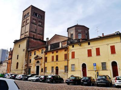 A cobblestone street lined with parked cars, featuring historic yellow buildings with red shutters and a prominent brick bell tower (Guelph Tower) alongside a domed structure, under an overcast sky.