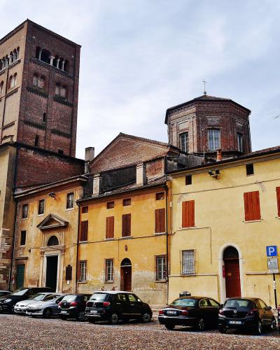 A cobblestone street lined with parked cars, featuring historic yellow buildings with red shutters and a prominent brick bell tower (Guelph Tower) alongside a domed structure, under an overcast sky.