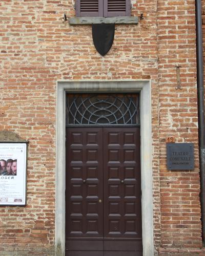 The image shows the entrance to a brick building with a plaque reading "TEATRO COMUNALE DEGLI OSCURI" and a poster for "Accademia degli Oscuri," located at number 12.