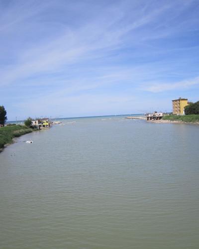 A wide river mouth flowing into the sea under a blue sky, with a paved path and trees on the left bank and buildings on the right bank.