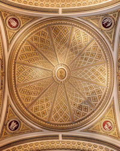 An ornate, gilded ceiling with a central circular medallion, radiating diamond-patterned coffers, and surrounding stucco reliefs and painted roundels.
