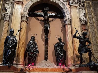 The image shows an interior religious sculpture group featuring a crucified Christ on a cross, flanked by statues of Mary, John the Evangelist, and a soldier (likely Longinus), set within an ornate architectural niche with columns and decorative w