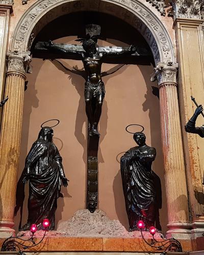 The image shows an interior religious sculpture group featuring a crucified Christ on a cross, flanked by statues of Mary, John the Evangelist, and a soldier (likely Longinus), set within an ornate architectural niche with columns and decorative w