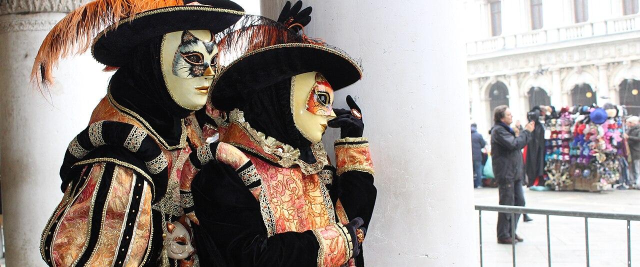 Two masked figures in Venetian carnival costumes under the Doge's Palace arcade in the Piazzetta